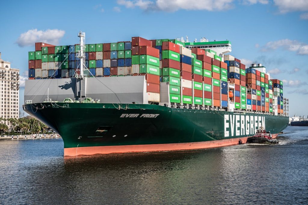A large container ship, the Ever Front, being guided by a tugboat in a busy seaport.